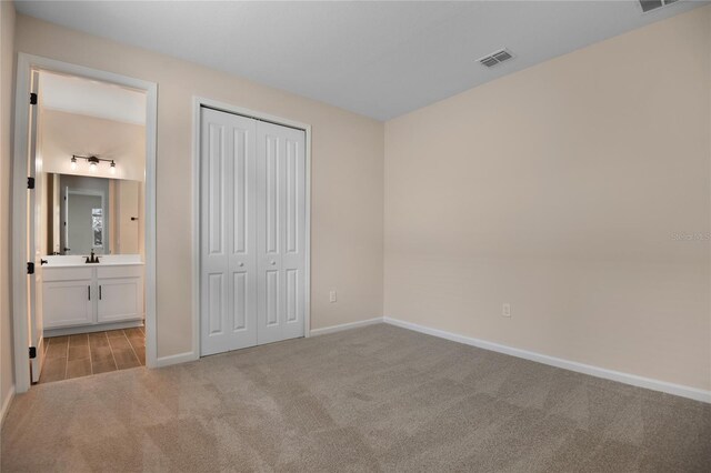 unfurnished bedroom featuring sink, ensuite bath, light colored carpet, and a closet