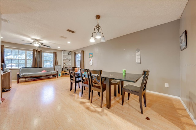 dining room featuring light wood-type flooring, ceiling fan with notable chandelier, and a textured ceiling