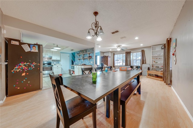 dining area featuring a textured ceiling, ceiling fan with notable chandelier, and light wood-type flooring