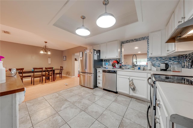 kitchen featuring a tray ceiling, light hardwood / wood-style flooring, stainless steel appliances, and tasteful backsplash