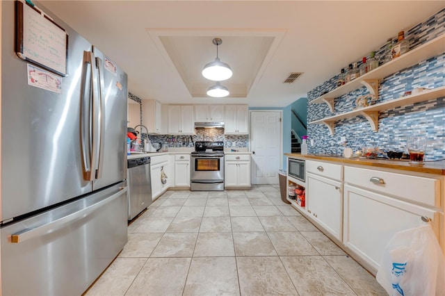 kitchen with light tile patterned floors, stainless steel appliances, decorative backsplash, pendant lighting, and a raised ceiling