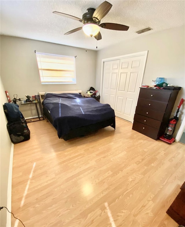 bedroom with a closet, a textured ceiling, ceiling fan, and light wood-type flooring