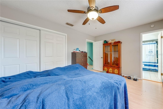 bedroom featuring a closet, ensuite bath, light hardwood / wood-style floors, a textured ceiling, and ceiling fan