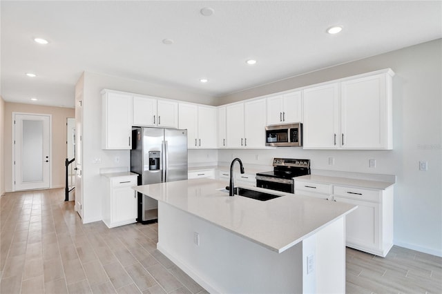 kitchen with sink, appliances with stainless steel finishes, white cabinetry, an island with sink, and light wood-type flooring