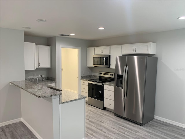 kitchen with appliances with stainless steel finishes, white cabinets, kitchen peninsula, light stone countertops, and light wood-type flooring