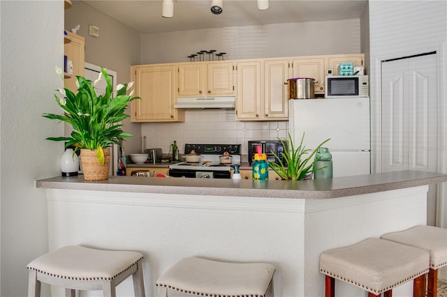 kitchen with white appliances, a breakfast bar, kitchen peninsula, and tasteful backsplash