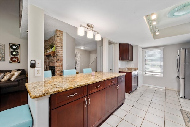 kitchen with light stone countertops, light tile patterned floors, stainless steel fridge, and a brick fireplace