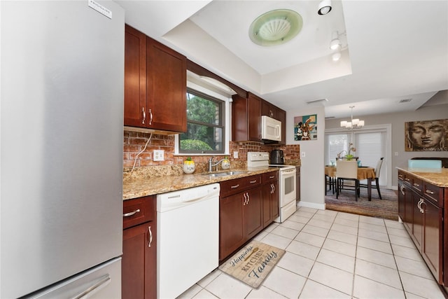 kitchen featuring white appliances, light tile patterned floors, decorative backsplash, a tray ceiling, and a notable chandelier