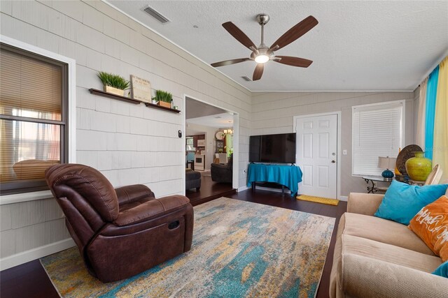 living room featuring dark wood-type flooring, ceiling fan, vaulted ceiling, and a textured ceiling