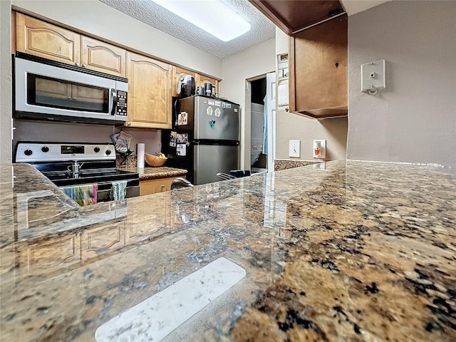 kitchen with stainless steel appliances, stone counters, and a textured ceiling