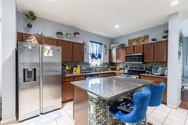 kitchen with appliances with stainless steel finishes, backsplash, light hardwood / wood-style floors, dark stone countertops, and a center island