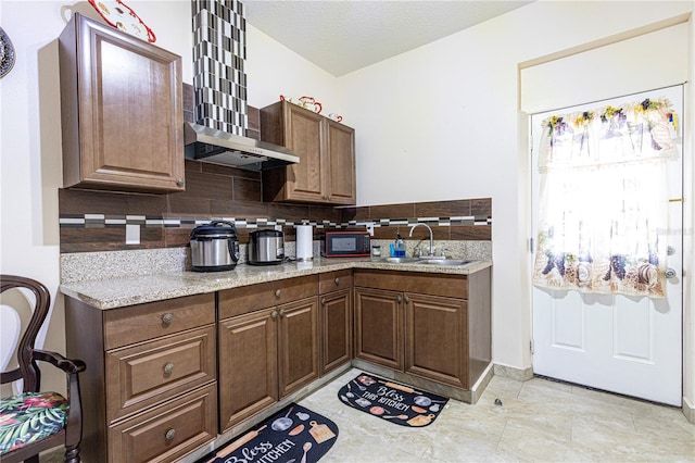 kitchen with sink, backsplash, light stone countertops, and wall chimney range hood