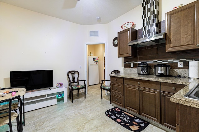 kitchen with white refrigerator, wall chimney range hood, dark brown cabinets, backsplash, and light tile patterned floors