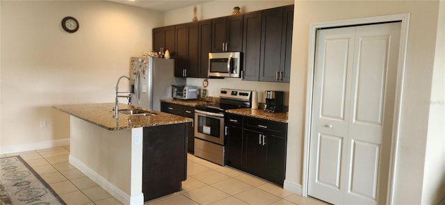 kitchen with light tile patterned flooring, sink, stainless steel appliances, and an island with sink