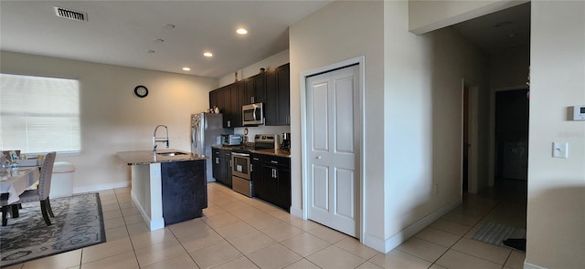 kitchen with stainless steel appliances, an island with sink, stone countertops, light tile patterned flooring, and sink