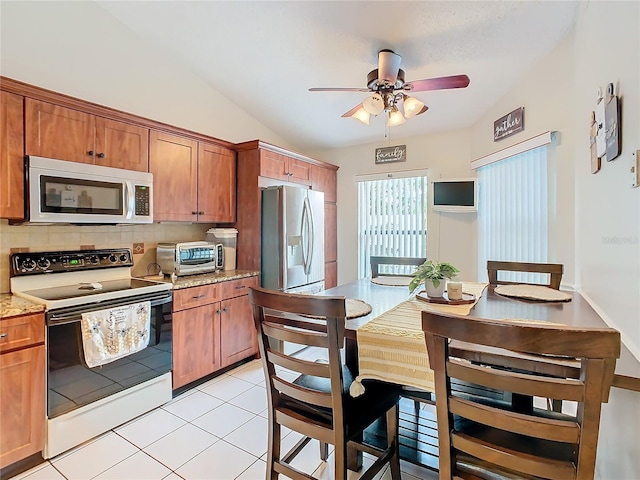 kitchen with light tile patterned flooring, tasteful backsplash, vaulted ceiling, stainless steel appliances, and light stone countertops