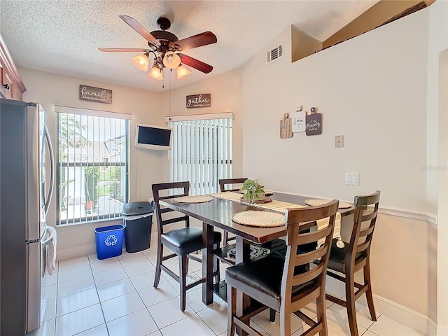 tiled dining room featuring ceiling fan, vaulted ceiling, and a textured ceiling