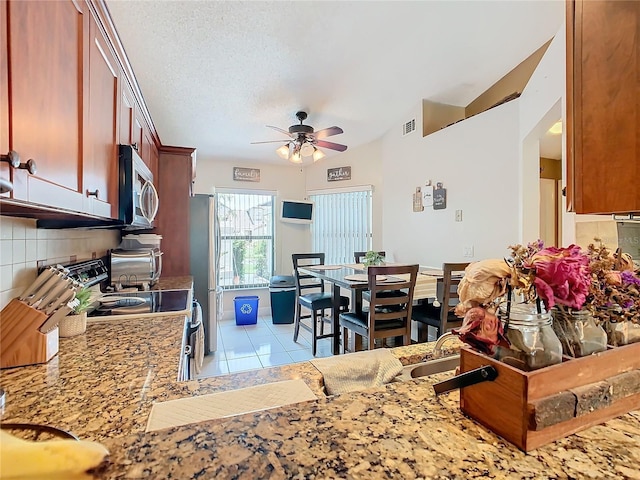 kitchen featuring light tile patterned floors, kitchen peninsula, ceiling fan, stainless steel appliances, and decorative backsplash