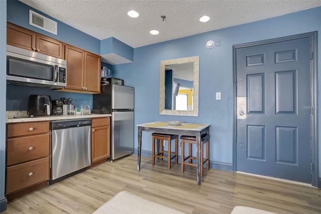 kitchen featuring stainless steel appliances, sink, a textured ceiling, and light hardwood / wood-style flooring