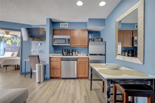 kitchen with ceiling fan, stainless steel appliances, a textured ceiling, and light hardwood / wood-style flooring