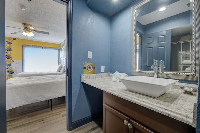 bathroom with hardwood / wood-style flooring, ceiling fan, vanity, and a textured ceiling