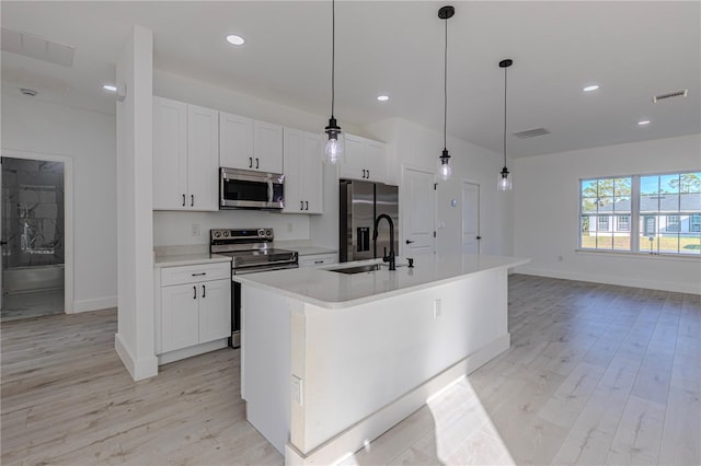 kitchen with stainless steel appliances, decorative light fixtures, light hardwood / wood-style flooring, a center island with sink, and white cabinetry