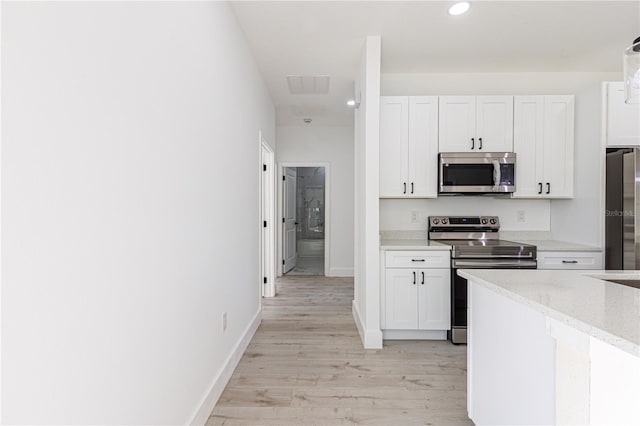 kitchen featuring light stone counters, white cabinets, light wood-type flooring, and appliances with stainless steel finishes