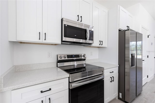 kitchen featuring light hardwood / wood-style floors, light stone counters, white cabinetry, and appliances with stainless steel finishes