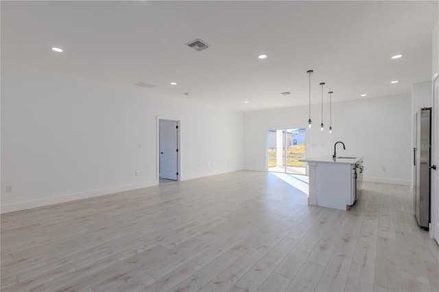 interior space featuring sink, a center island with sink, light hardwood / wood-style flooring, stainless steel refrigerator, and hanging light fixtures