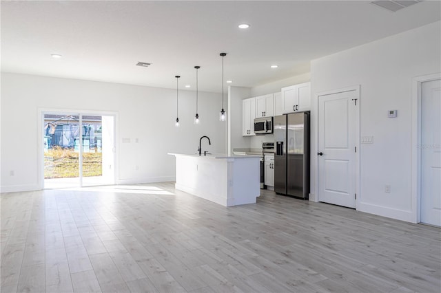 kitchen with stainless steel appliances, a center island with sink, light hardwood / wood-style flooring, white cabinets, and hanging light fixtures