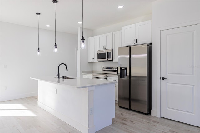 kitchen featuring stainless steel appliances, sink, decorative light fixtures, a center island with sink, and white cabinets