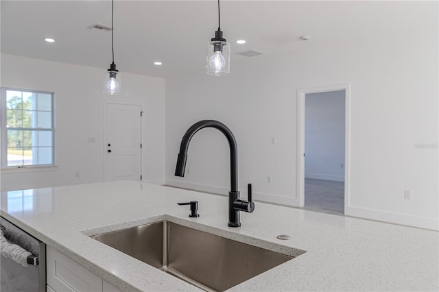 kitchen with light stone countertops, hanging light fixtures, dishwasher, and sink