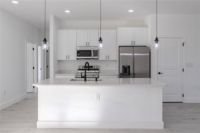 kitchen featuring a center island with sink, white cabinetry, stainless steel appliances, and hanging light fixtures