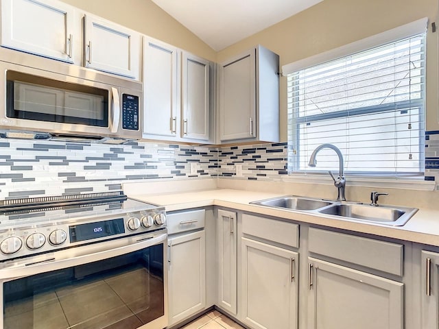 kitchen featuring lofted ceiling, sink, light tile patterned floors, appliances with stainless steel finishes, and decorative backsplash