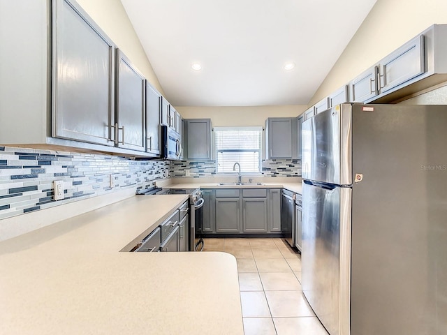 kitchen featuring lofted ceiling, sink, appliances with stainless steel finishes, light tile patterned flooring, and decorative backsplash