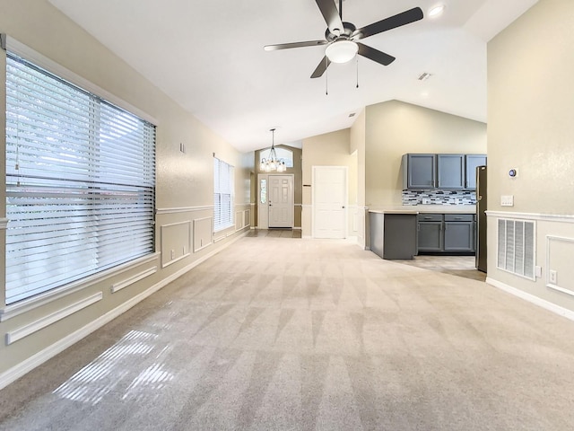 unfurnished living room featuring vaulted ceiling, ceiling fan with notable chandelier, and light colored carpet