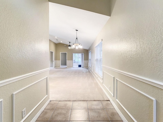 hall featuring a notable chandelier, vaulted ceiling, and light colored carpet