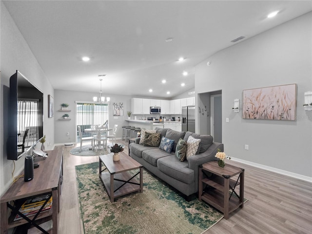 living room with an inviting chandelier, high vaulted ceiling, and light hardwood / wood-style flooring