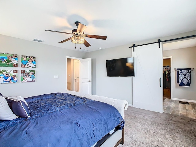 carpeted bedroom featuring a walk in closet, visible vents, ceiling fan, and a barn door