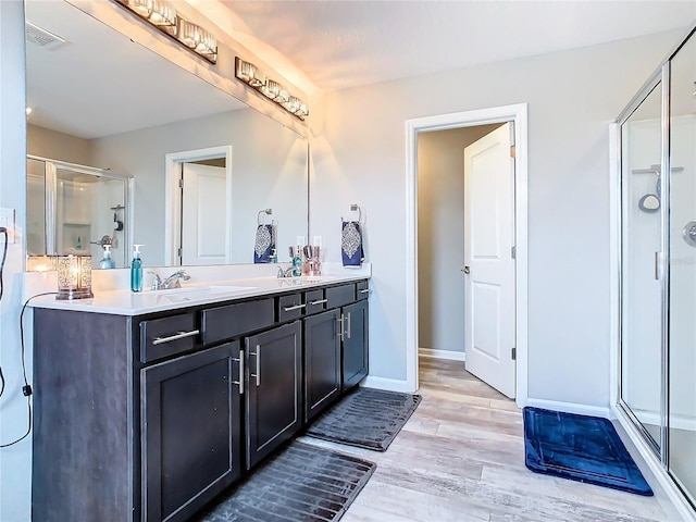 bathroom with wood finished floors, a sink, visible vents, baseboards, and a stall shower