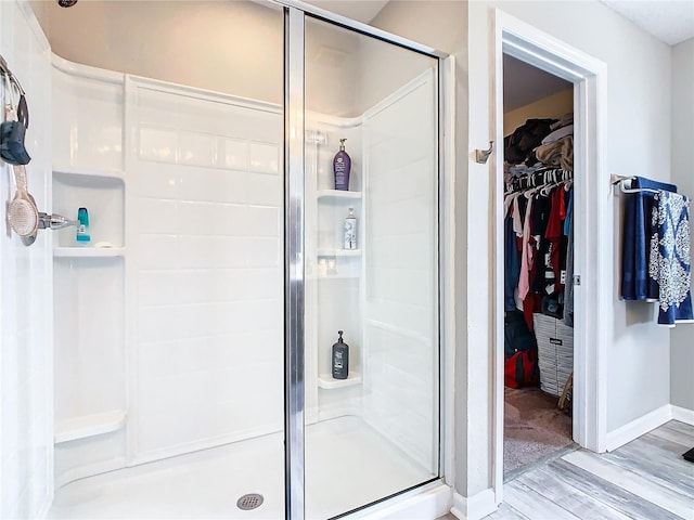 bathroom featuring a spacious closet, a stall shower, wood finished floors, and baseboards