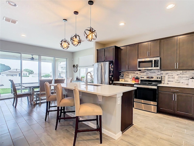 kitchen with a breakfast bar area, stainless steel appliances, visible vents, decorative backsplash, and dark brown cabinetry