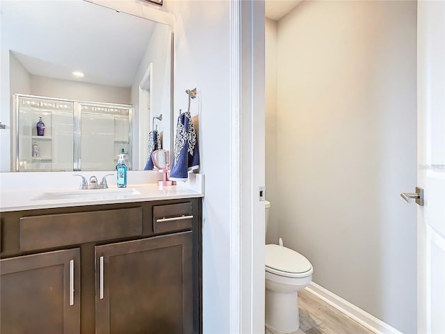 full bathroom featuring toilet, a stall shower, vanity, wood finished floors, and baseboards