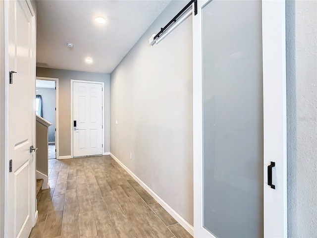 hallway with a barn door, light wood-style flooring, and baseboards