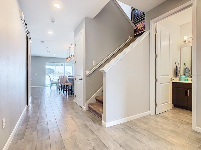 hallway with a barn door, recessed lighting, baseboards, stairs, and light wood-style floors