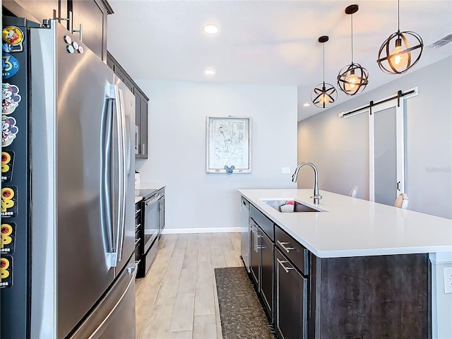 kitchen featuring a barn door, a center island with sink, appliances with stainless steel finishes, light countertops, and a sink