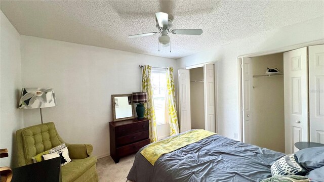 bedroom featuring ceiling fan, a textured ceiling, multiple closets, and light carpet