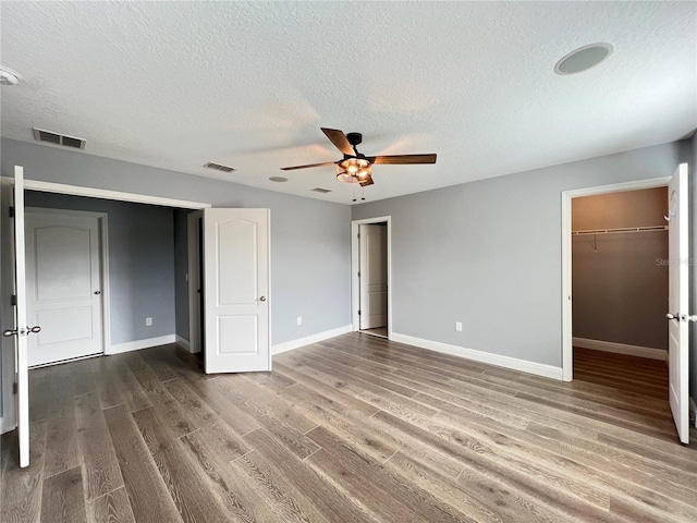 unfurnished bedroom with hardwood / wood-style flooring, ceiling fan, a textured ceiling, a walk in closet, and a closet