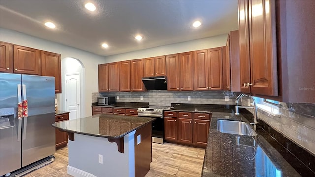 kitchen with sink, dark stone countertops, appliances with stainless steel finishes, a kitchen breakfast bar, and exhaust hood