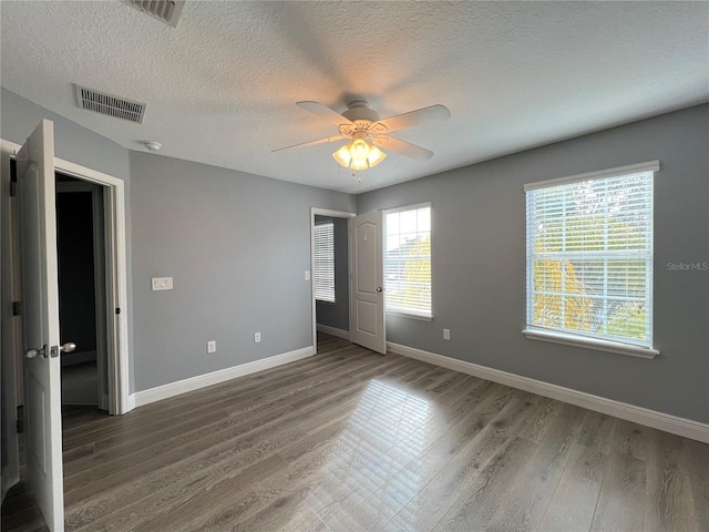 unfurnished bedroom with multiple windows, dark hardwood / wood-style flooring, a textured ceiling, and ceiling fan